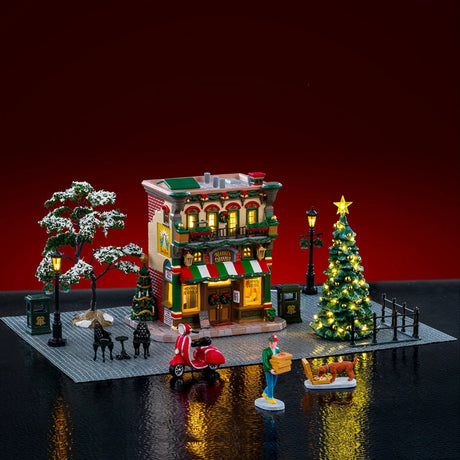 This is a lifestyle image showing this Lemax house set on a fake background. It was designed to look like a tall pizzeria on a stone patio. There are some snowy trees, as well as a lighted tree. There are a few garbage bins, a moped, some lampposts, a patio dining set and a boy carrying a bunch of boxes of pizza. It looks like he accidentally dropped one and there's a dog eating from the box.