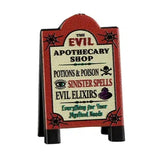 This Lemax sign is a burnt orange color, as well as a pale yellow, black and dark green. It reads "The Evil Apothecary Shop. Potions & poison. Sinister spells. Evil elixirs. Everything for your mystical needs."