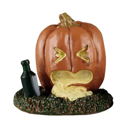 This Lemax accessory looks like a jack-o-lantern on a grassy patch. There's a green bottle on the ground next to the pumpkin. The pumpkin looks like it threw up.