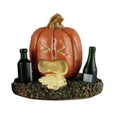 This Lemax accessory looks like a jack-o-lantern on a grassy patch. There's a green bottle on the left of the pumpkin and on the right. This pumpkin looks like it has thrown up.