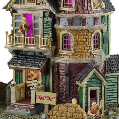 This is an up close view of the house. The house is painted a bunch of different unique colors like forest green, bronze yellow, black and brown and has a purple glow coming from inside.