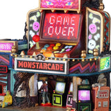 This is an up close view of the lighted building. There's someone inside playing an arcade game. There's a monster sitting on the sidewalk. On the outside of the building, there are some games and an orange-ish pink colored token machine. On top of the token machine, there's a skeleton laying down.