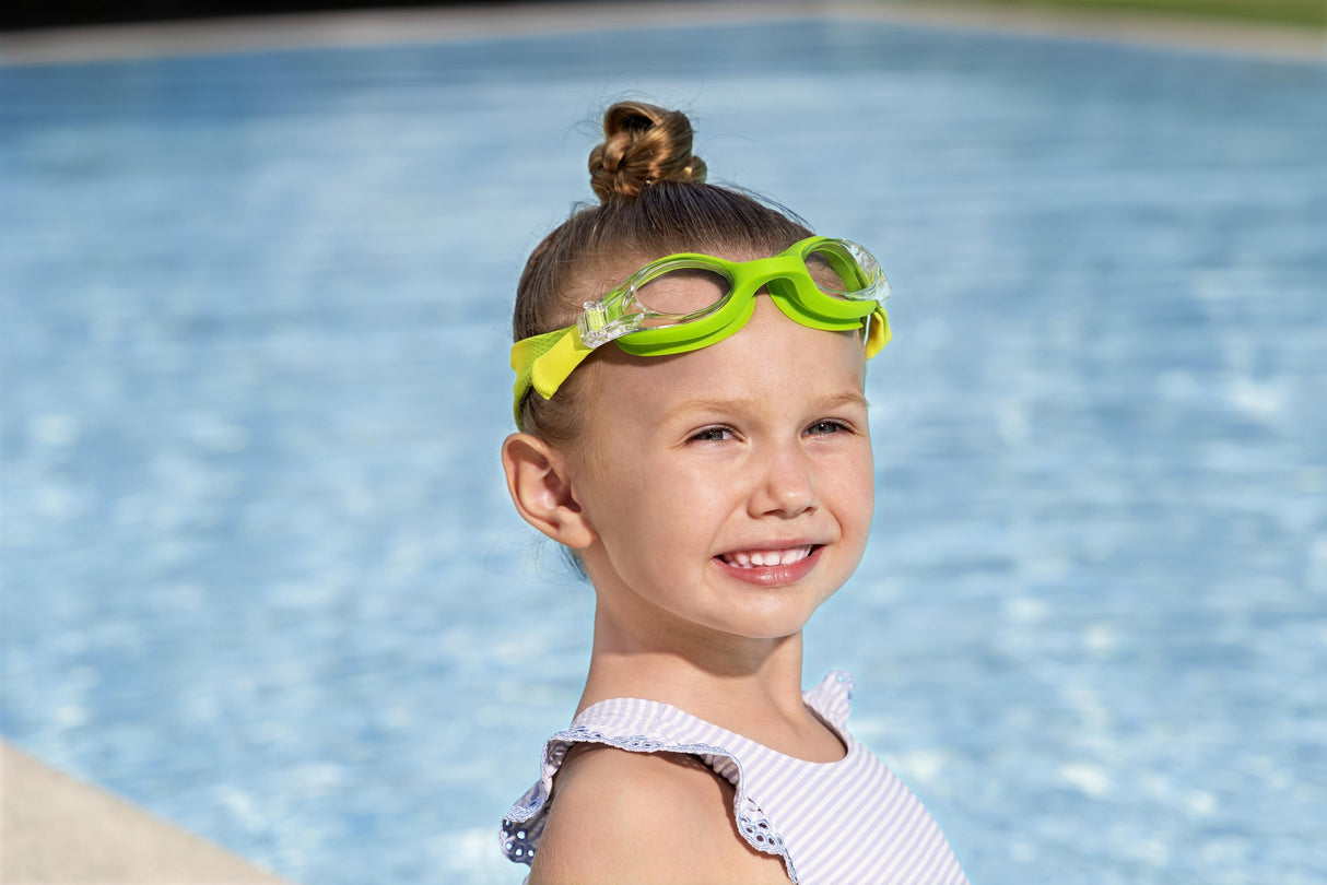 This is a lifestyle image showing a young girl with the lime green goggles on her forehead near a pool.