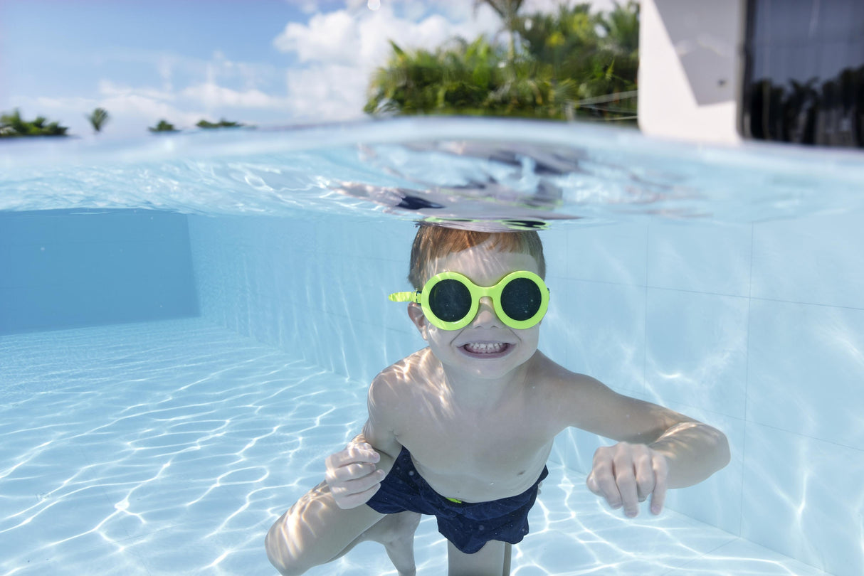 This is a lifestyle image showing a young boy smiling underwater wearing the neon yellow colored goggles.