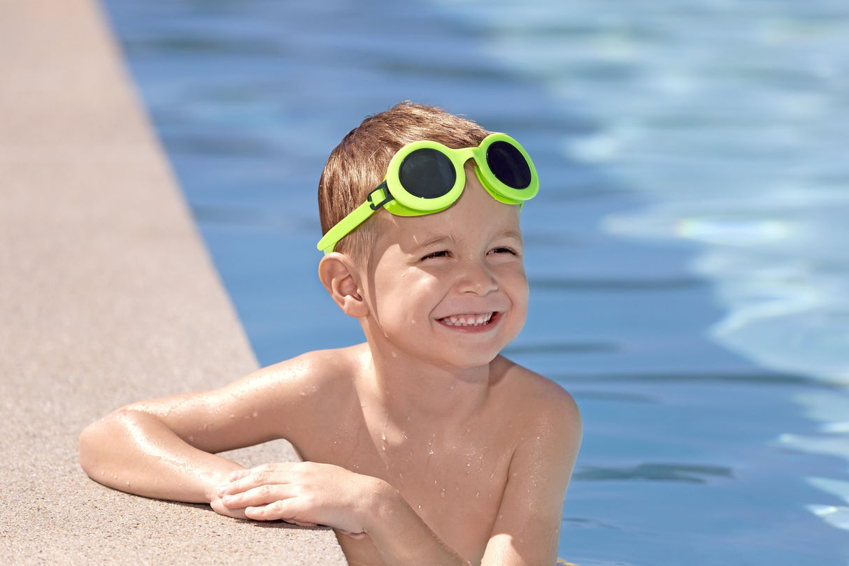 This is a lifestyle image showing a young boy smiling at the camera with the neon yellow goggles around his forehead.