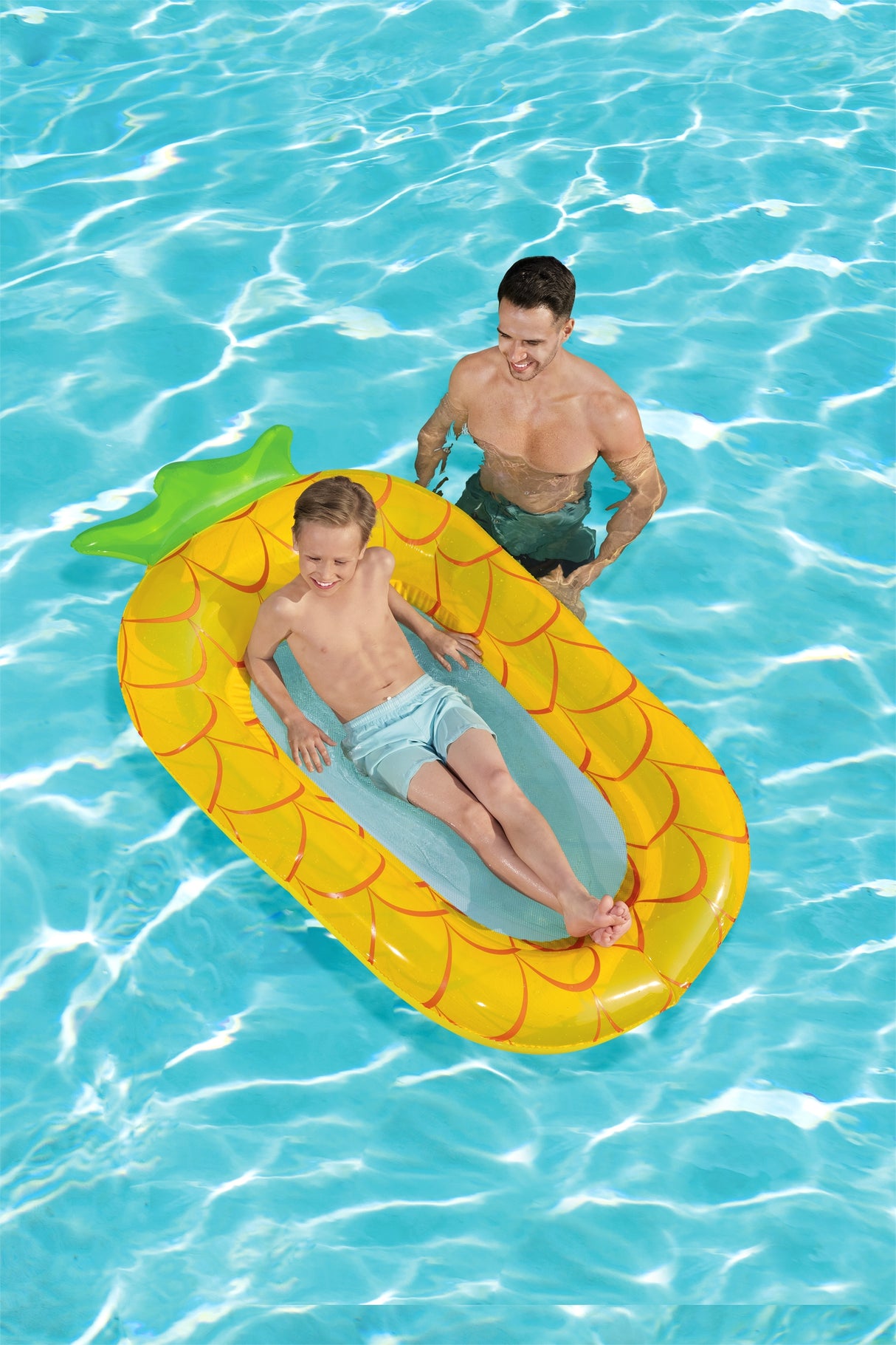 This is a lifestyle image showing a young boy resting inside the pineapple float while his dad floats nearby.