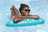 This is a lifestyle image showing a woman laying on her stomach on the hammock in the pool.