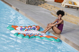 This is a lifestyle image showing a woman sitting on the side of the pool and resting her feet on the pool float.