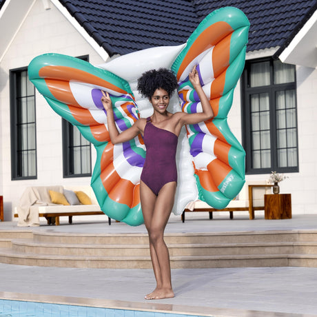 This is a lifestyle image showing a woman using this butterfly shaped pool float as wings behind her.