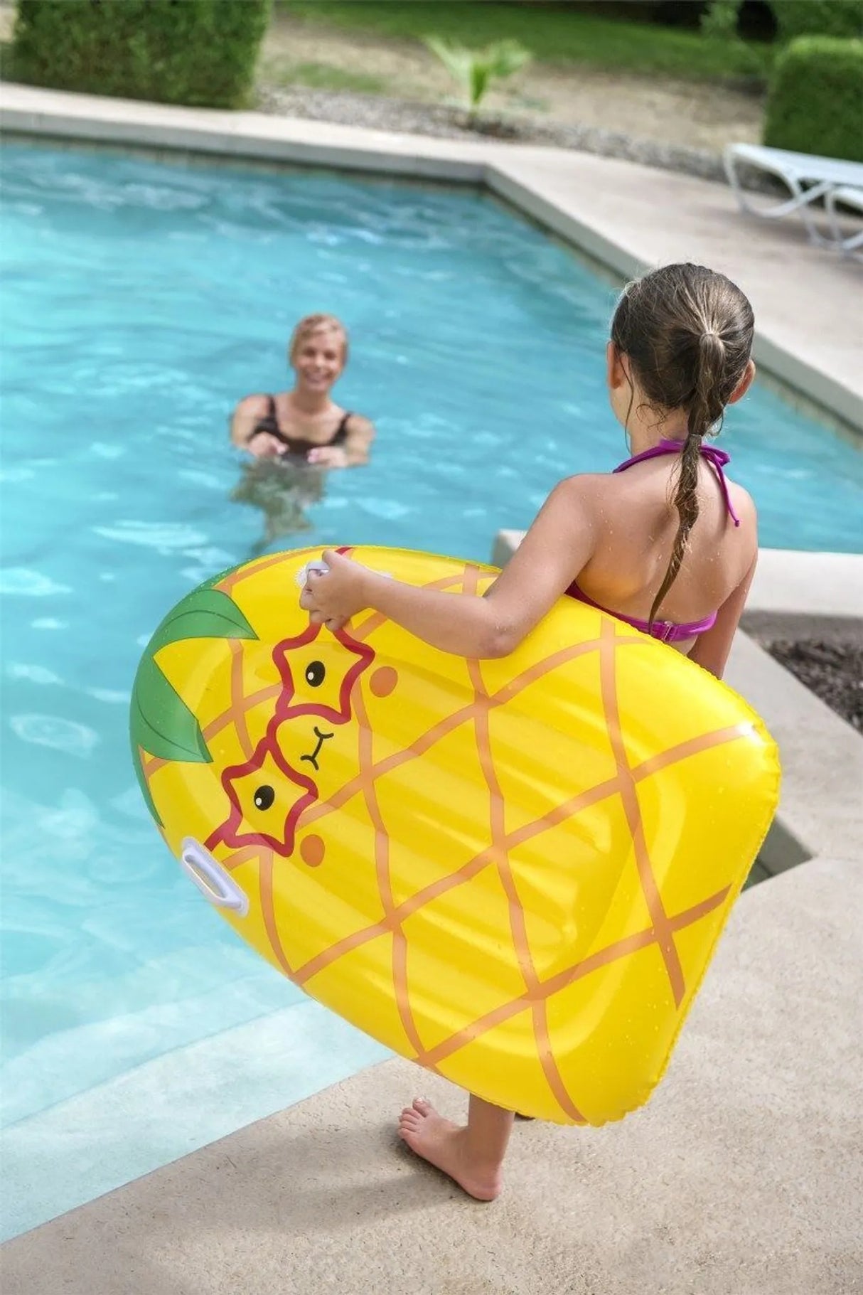 This is a lifestyle image showing a little girl holding the pineapple surf rider float while heading into the water.