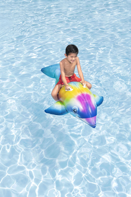 This is a lifestyle image showing a young boy riding on the dolphin float in the pool.