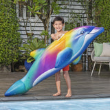 This is a lifestyle image showing a young boy holding a dolphin pool ride-on while standing next to a pool.