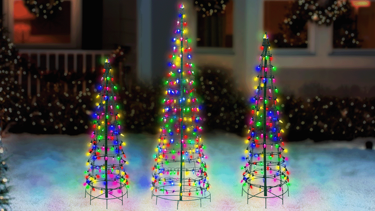 This animated image shows three black frame wire cone trees pre-lit with multi-colored twinkling lights on a snowy lawn in front of a house decorated for Christmas.