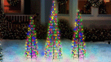 This animated image shows three black frame wire cone trees pre-lit with multi-colored twinkling lights on a snowy lawn in front of a house decorated for Christmas.