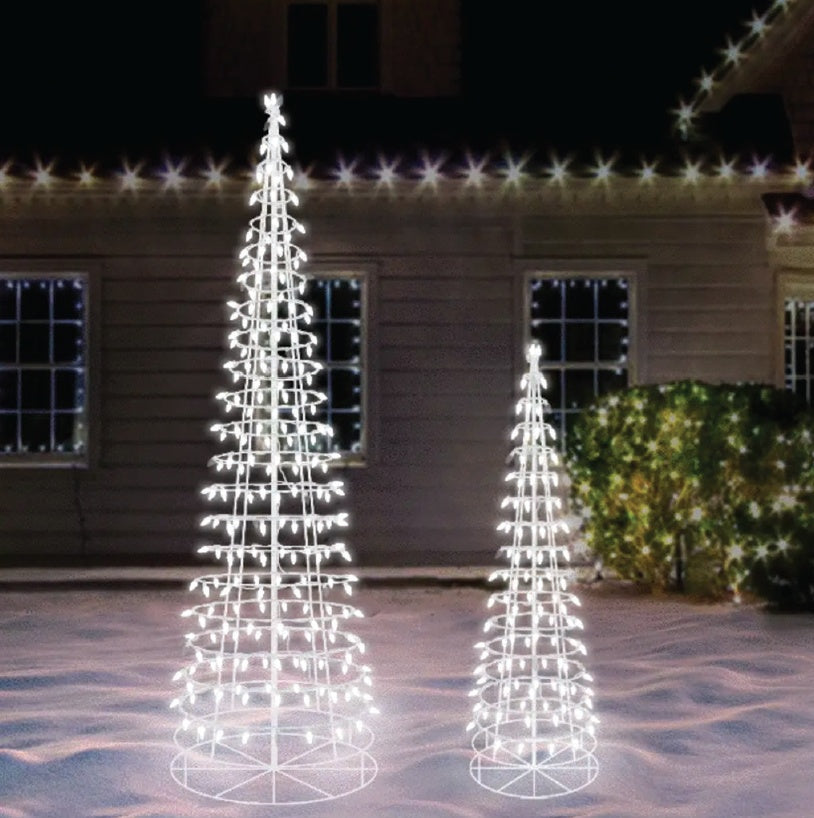 This is a lifestyle image showing two white wire cone trees of different sizes on a snowy lawn in front of a house.