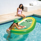 This is a lifestyle image showing a girl leaning on the avocado pool float in a pool while her friend sits on the edge of the pool watching.
