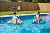 This is a lifestyle image showing two young kids riding the jet fighter floats in a pool. They're both shooting the water blasters at each other.