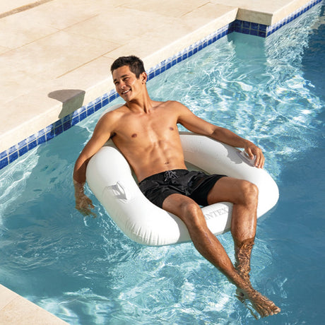 This is a lifestyle image showing a man sitting in the white inflatable chair in a pool.