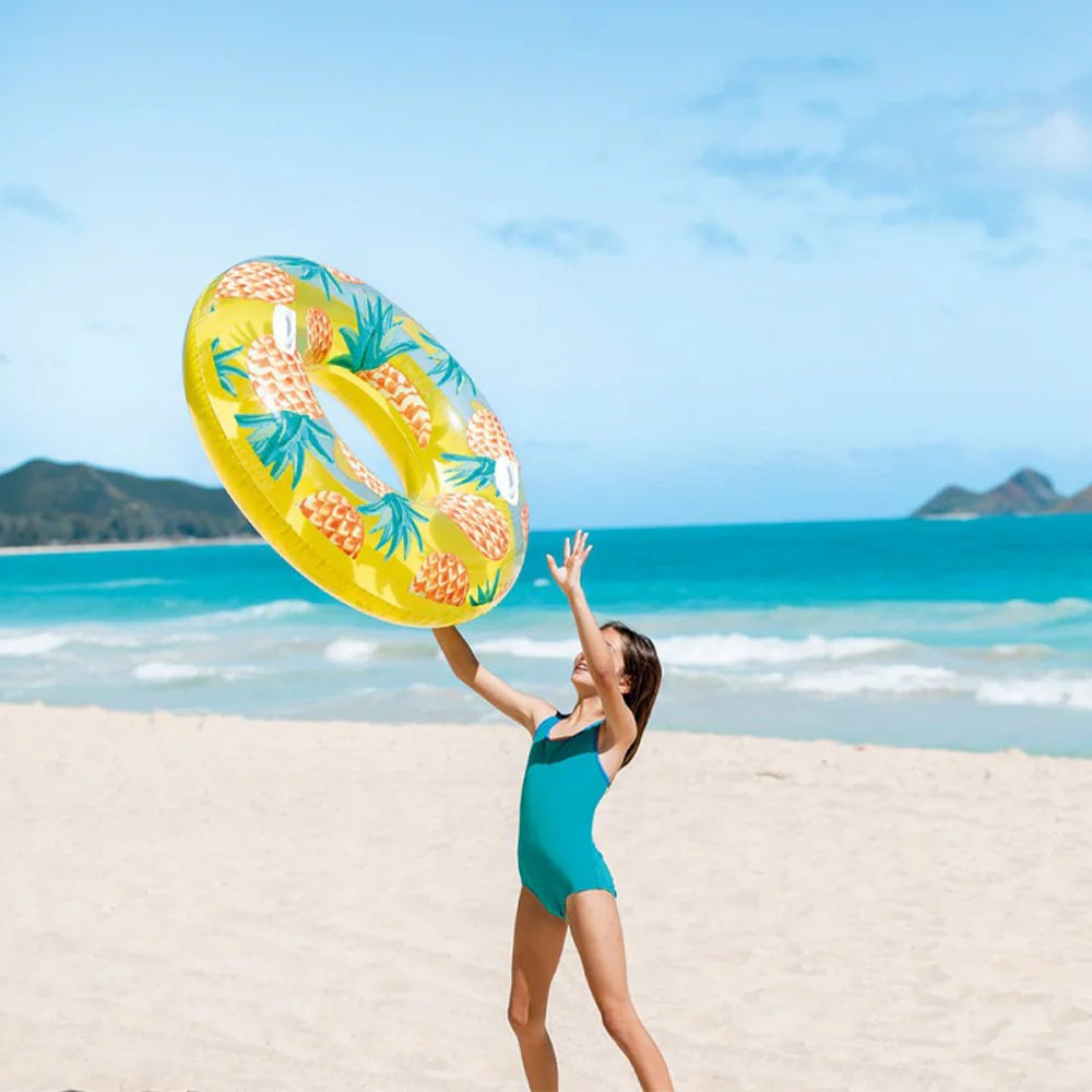 This is a lifestyle image showing a young girl on the beach, throwing the pineapple inner tube in the air.