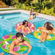 This is a lifestyle image showing three people floating in the fruit themed inner tubes in a pool while their friend looks on in the connected hot tub.