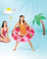 This is a lifestyle image showing a young girl standing inside the strawberry inner tube on a set that is designed to look like a beach made out of paper.