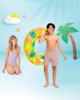 This is a lifestyle image showing a young boy holding the pineapple inner tube on a set that is designed to look like a beach made out of paper.