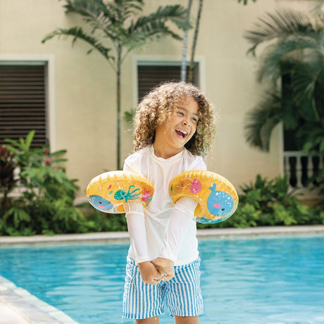 This is a lifestyle image showing a young child wearing both of these floaties on their arms on the side of a pool.
