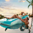 This is a lifestyle image showing a woman sitting on the inflatable chair in a pool while a man rests his arms on it.