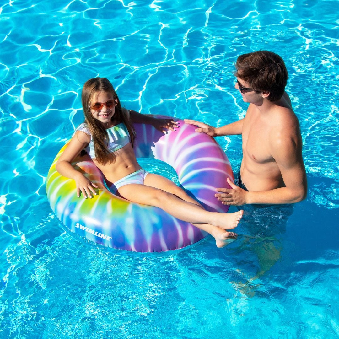 This image shows a little girl floating inside the swim ring in a pool while her dad looks on.