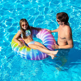 This image shows a little girl floating inside the swim ring in a pool while her dad looks on.