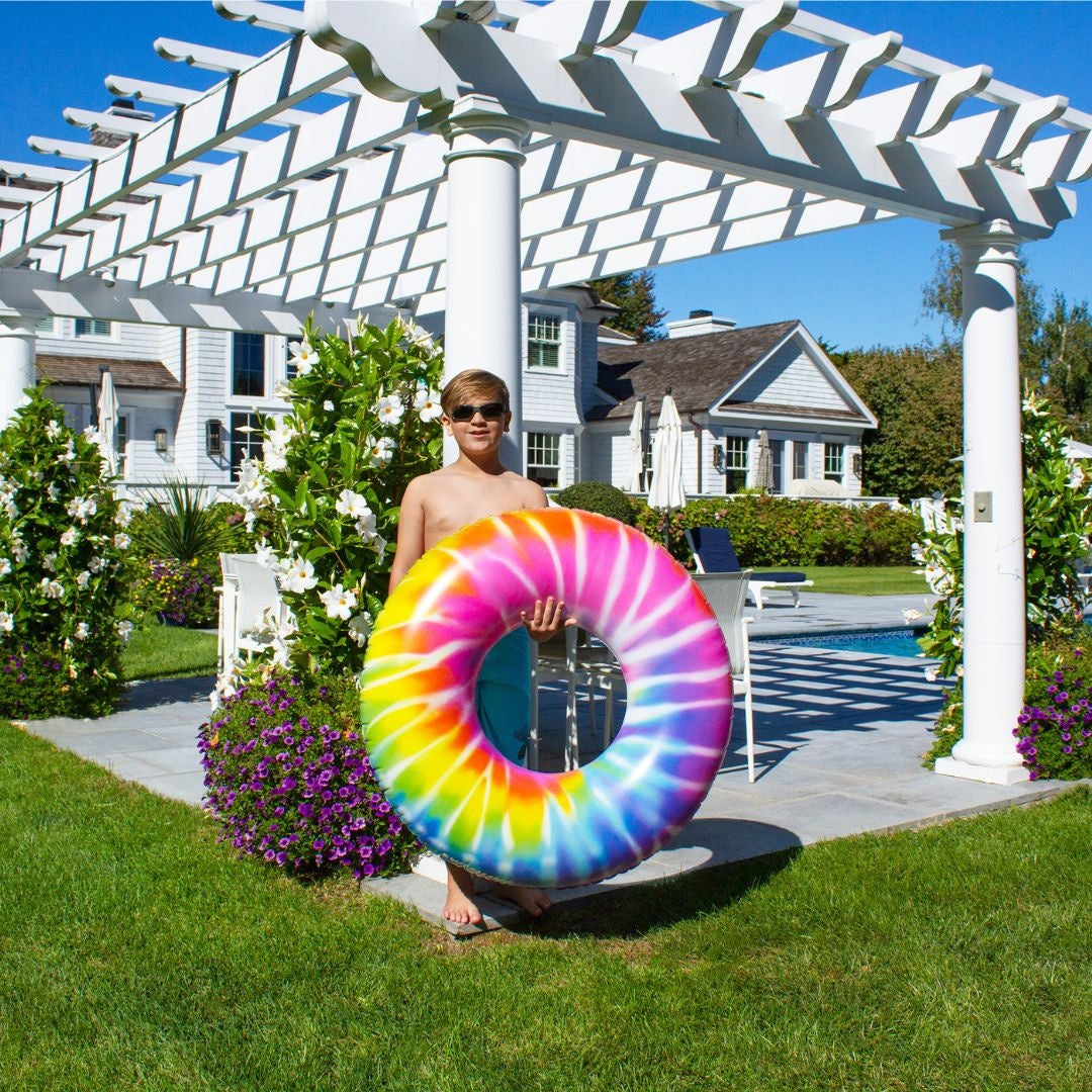 This is a lifestyle image showing a young boy holding the spiral tie dye inner tube while standing beside a gazebo in a grassy backyard.