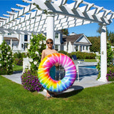 This is a lifestyle image showing a young boy holding the spiral tie dye inner tube while standing beside a gazebo in a grassy backyard.