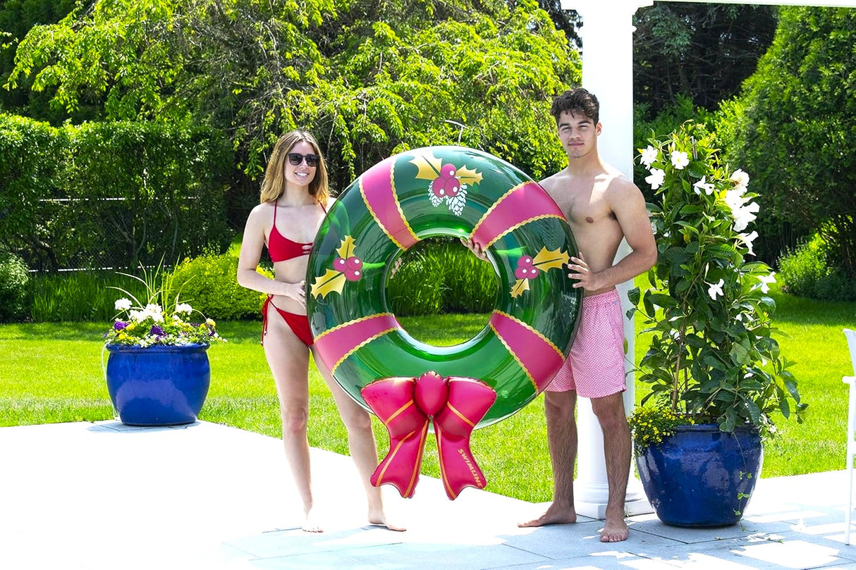 This is a lifestyle image showing a young woman and a young man holding the wreath inner tube on a pool deck.