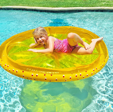 This is a lifestyle image showing a little girl smiling and posing on this yellow lemon slice pool float.