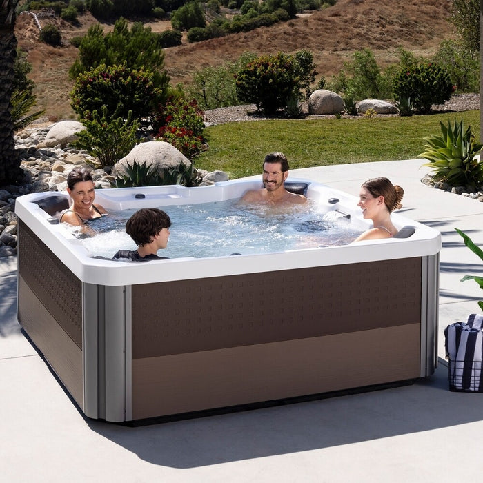 This is a lifestyle image showing four people inside of the hot tub in an exotic looking backyard.