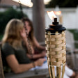 This is a lifestyle image showing the natural bamboo tiki torch in use while two girls chat on a porch swing.