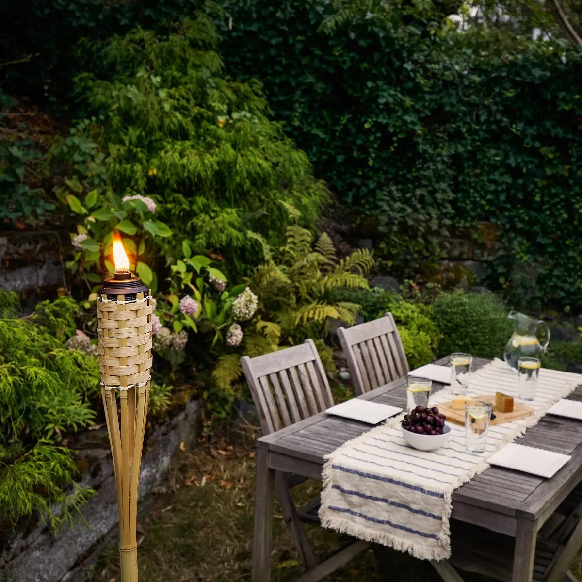 This is a lifestyle image showing a tiki torch in use next to an outdoor table that is set up for four people.