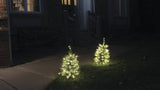 This is a lifestyle image showing the tree pre-lit artificial trees lining a pathway near a front door.