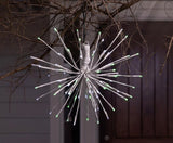 This is a lifestyle image showing this LED starburst decoration hanging from a tree. The lights on it are green and pure white.