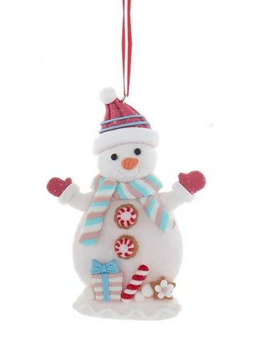 This ornament is a snowman with a red knit hat, red gloves, a light blue, grey and white striped scarf and peppermint candy buttons. Near the base of the snowman, there's a gift, a peppermint stick and a small flower.