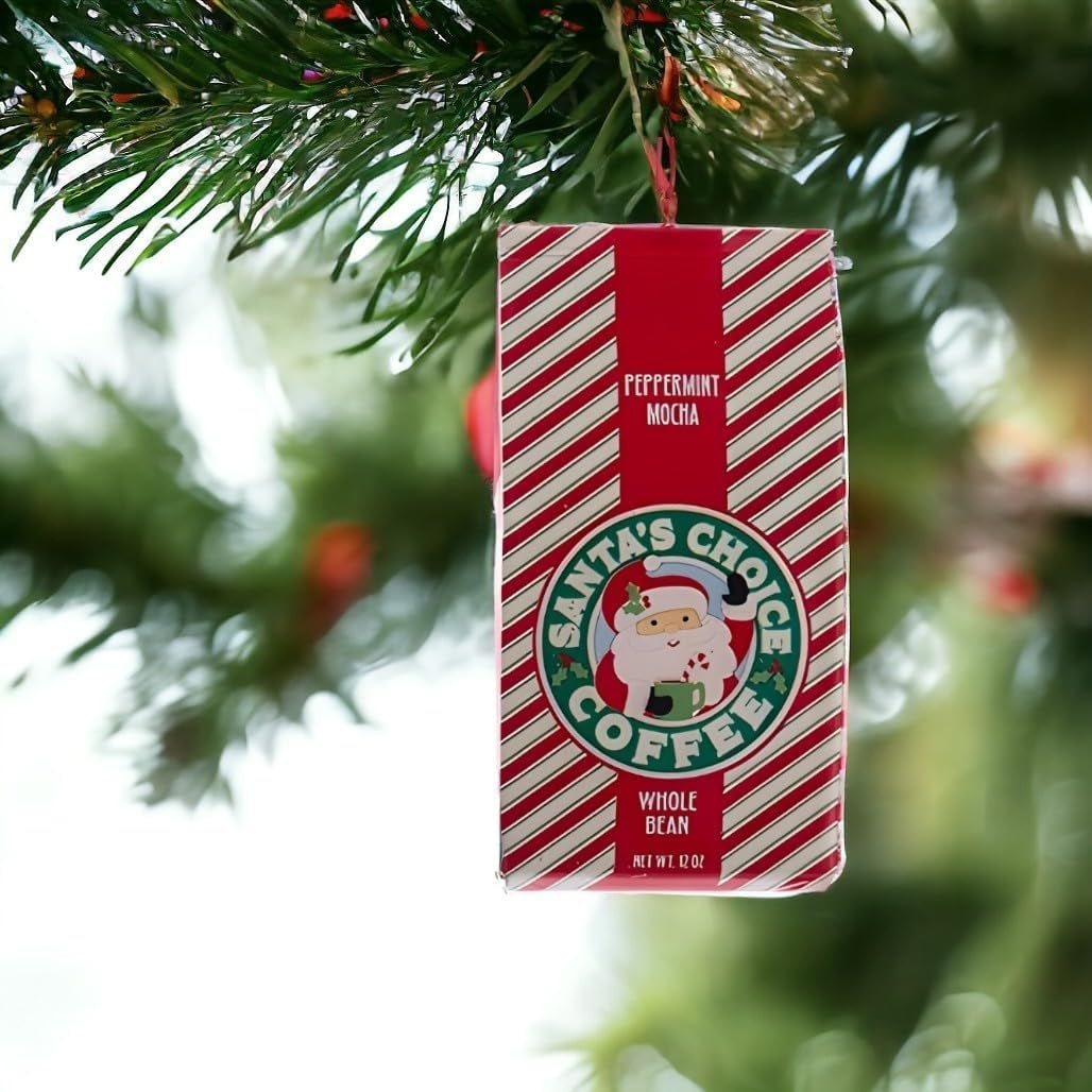 This is a lifestyle image showing the ornament hanging from a tree branch. This ornament was designed to look like a bag of coffee that is red and white striped and reads "Peppermint Mocha Santa's Choice Coffee Whole Bean."