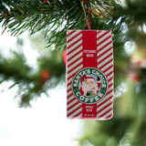 This is a lifestyle image showing the ornament hanging from a tree branch. This ornament was designed to look like a bag of coffee that is red and white striped and reads "Peppermint Mocha Santa's Choice Coffee Whole Bean."