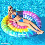 This is a lifestyle image showing a woman laying on this circular pool inflatable. The design on this pool lounger is supposed to look like a swirled tie dye design.