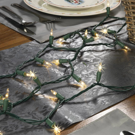 This is a lifestyle image showing these twinkling warm white lights on a green wire on a gray table runner.