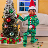 This is a lifestyle image showing a Scout Elf wearing the pajamas while decorating a small Christmas tree.