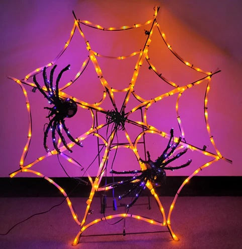 This image shows a Halloween decoration designed to look like an orange spider web with two black spiders on it. The spiders have purple twinkling lights on them.