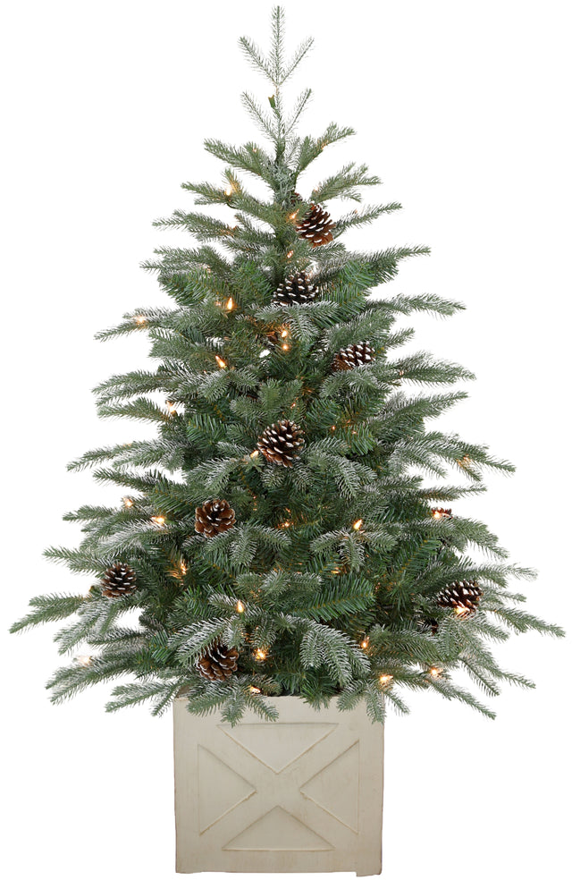 This image shows a fake fir tree plant with white, flocked tips, clear incandescent lights and pine cones. It's inside a square white washed base.