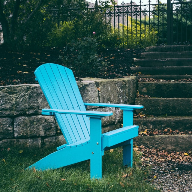 A light blue colored adirondack chair on some grass next to a stone walkway.