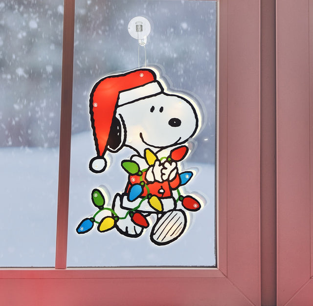 This is an up close view of this Snoopy decoration hanging in a window while it snows outside.
