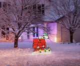 This is a lifestyle image showing the Snoopy doghouse decoration on a snowy front lawn decorated for Christmas.